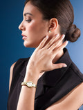 Profile view of a model elegantly touching her neck, showcasing the Saint Honoré Petit Palais gold watch on her wrist against a clean blue background.