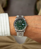 A lifestyle photograph of the Cerruti 1881 Chienti watch worn on a man's wrist, styled with a casual striped shirt and beige trousers, highlighting its everyday elegance and the reflection on its green dial face.