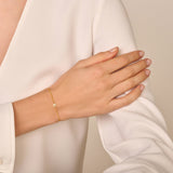 Thin gold-toned chain bracelet with a small, round, flat charm encrusted with clear sparkling stones.