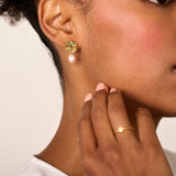 Gold-toned earring with a round, textured stud featuring an intricate design, from which an irregular off-white pearl dangles