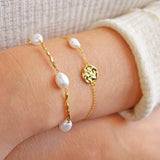 Gold-toned bracelet featuring irregular white pearls alternating with wavy, elongated links.
