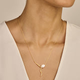 Gold-toned necklace with a thin chain and an abstract, wavy pendant featuring an irregular white pearl and small clear stones