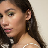 Gold-toned hoop earring with a small green gem, a long thin chain, and a shorter flat pointed dangle.