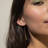 A single gold-toned drop earring with a hook, featuring a long, slender, tapered body with a chevron pattern.