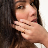 Thin, gold-toned ring with a textured band, featuring a small, irregular yellowish-orange gem and a tiny clear round stone.
