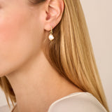 A single gold-toned hoop earring with tiny clear stones, suspending an irregular off-white baroque pearl.