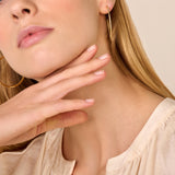 Two gold-toned hoop earrings with a fine textured surface. One earring is fully visible, the other is partially visible.