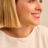 Silver-toned necklace featuring a thin chain and a curved bar pendant. Half of the bar is smooth, the other half is set with