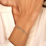 White plated bracelet with three delicate chains, two arch-shaped links, and a central link adorned with clear stones.