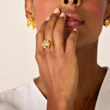 Gold-toned ring with a textured five-petal flower design, featuring a small clear crystal in its center.