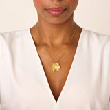 Gold-toned necklace with a thin chain and a six-petal flower pendant. The flower has textured petals and a small, clear round