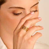 Gold-toned linear ring with multiple intertwined bands, one band features a row of small clear stones.
