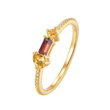 Gold-toned ring with a pear-shaped yellow stone, a rectangular dark red stone, a small square yellow stone, and pavé clear st