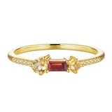 Gold-toned ring with a rectangular dark red stone, flanked by a pear and square light yellow stone, and clear pavé stones.