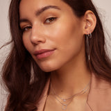 White-plated threader earring with a thin chain and a stone-encrusted bar hanging from the earlobe.