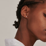 A single gold-toned stud earring with a small, round, clear stone set in gold-toned metal.