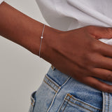 White-plated delicate chain bracelet featuring a single round clear stone in the middle.