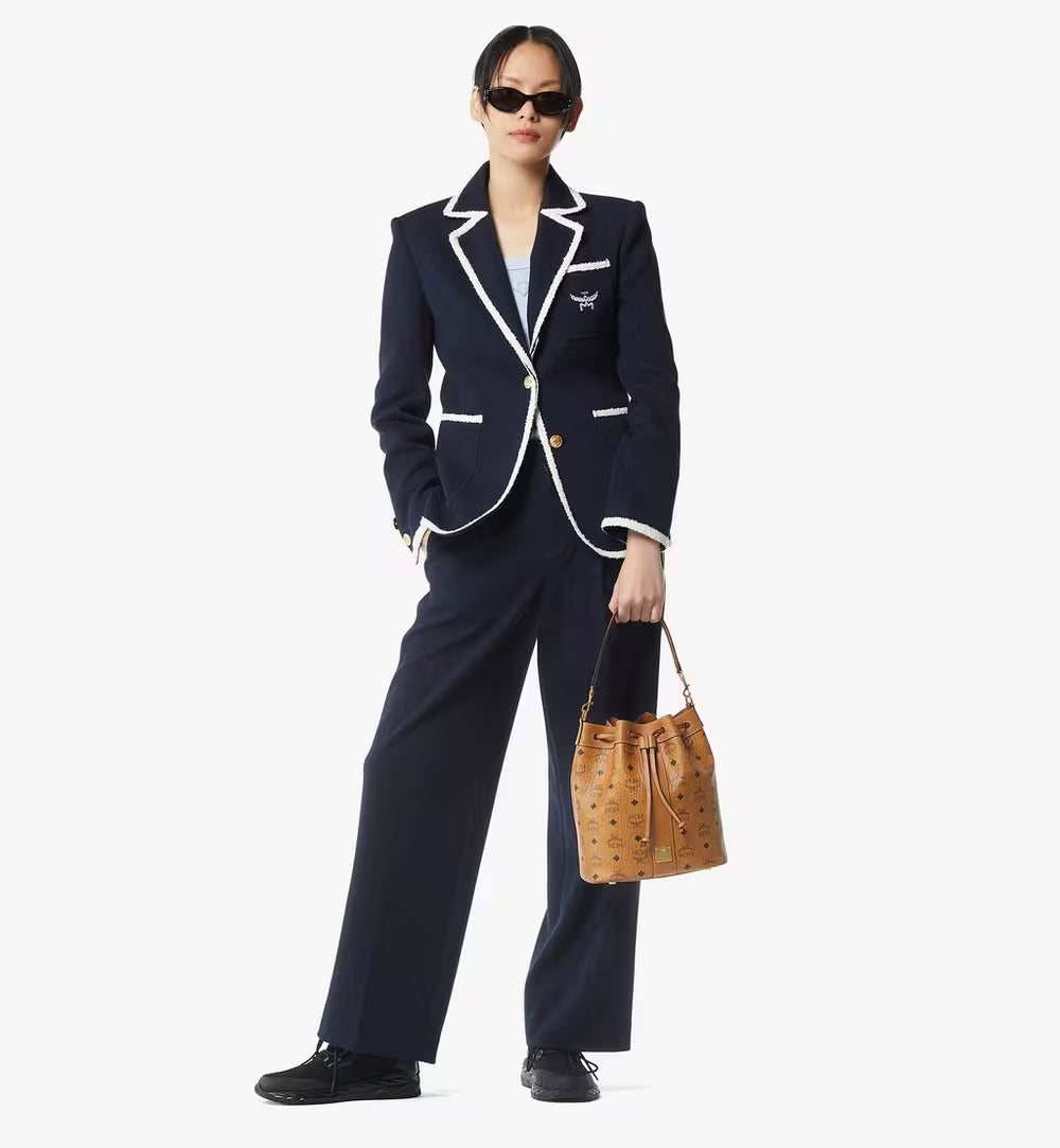 Woman in a navy suit with white trim holding a brown handbag on a white background.