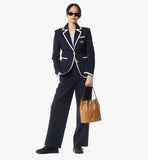 Woman in a navy suit with white trim holding a brown handbag on a white background.