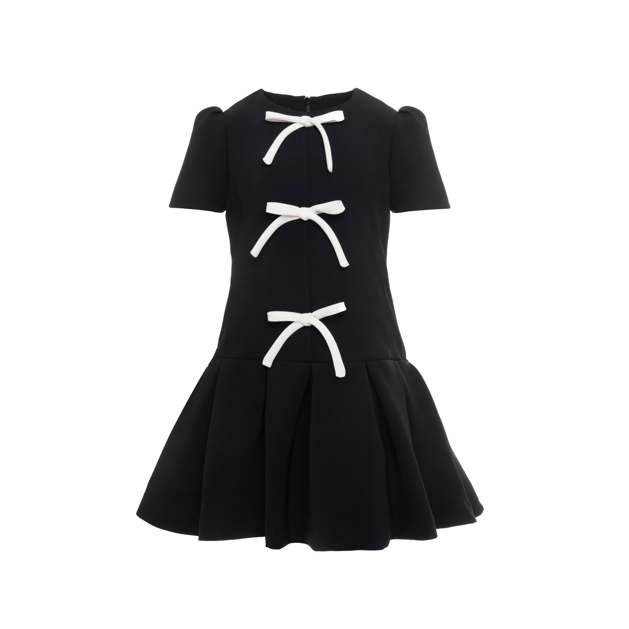 Black short-sleeved dress with a fitted bodice, three white decorative bows, and a pleated flared skirt.
