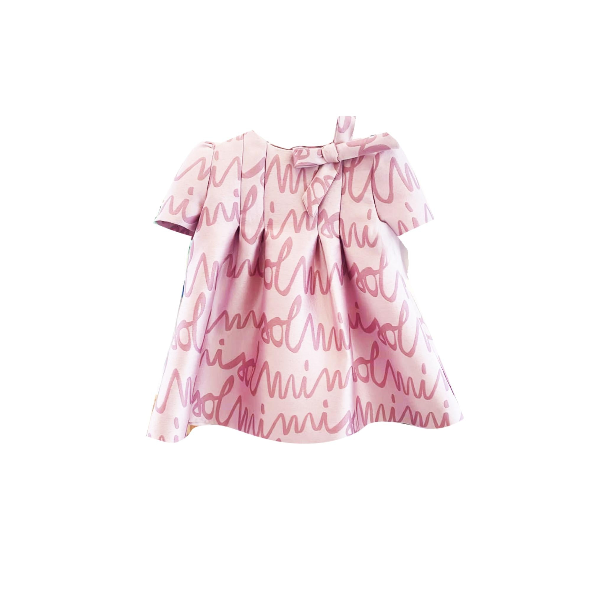 Pink short-sleeved dress with round neckline, pleated bodice, flared skirt, and all-over darker pink script pattern. Bow on l