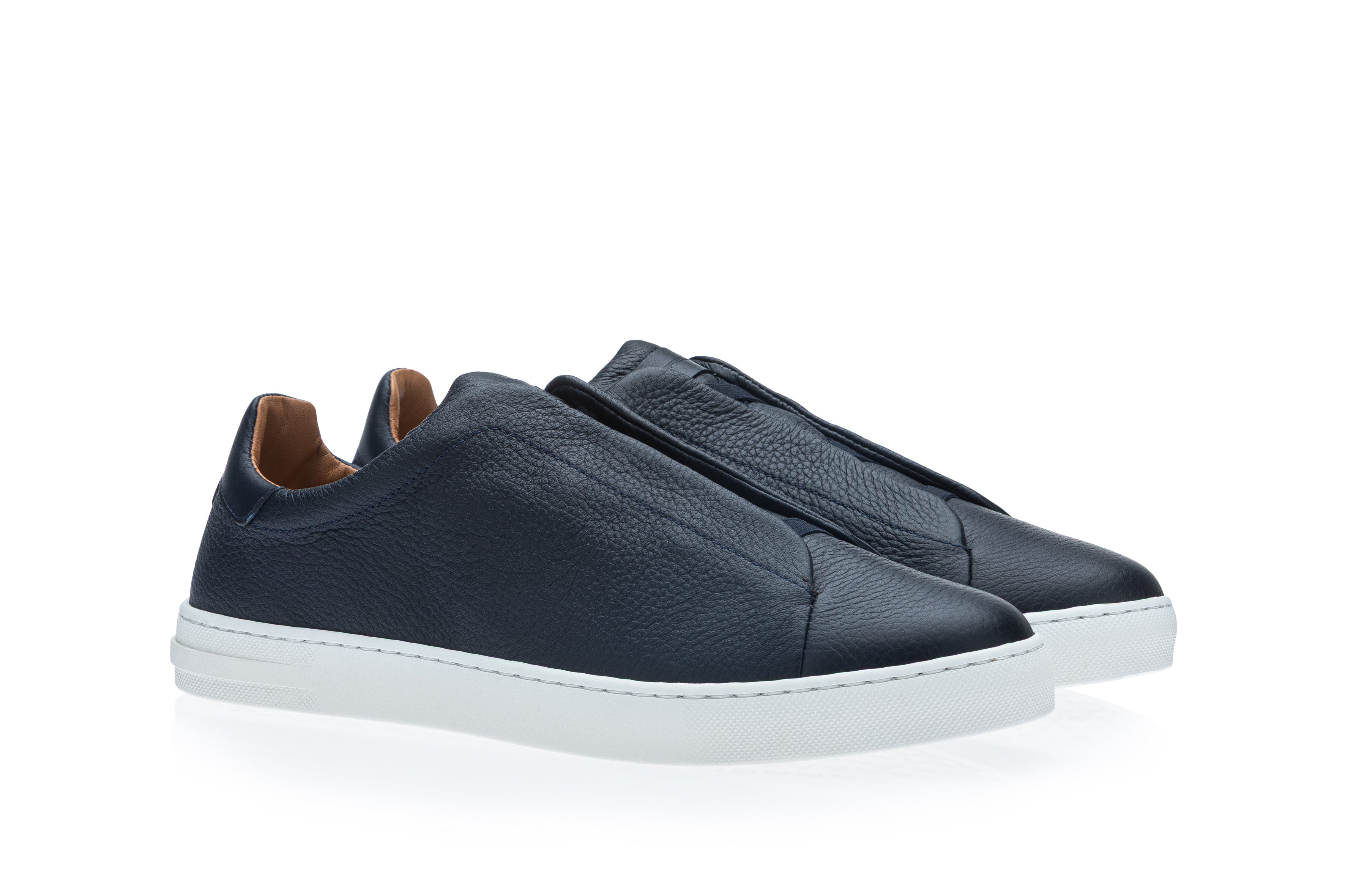 Pair of dark blue pebbled leather slip-on sneakers with white rubber soles and light brown inner heel lining.