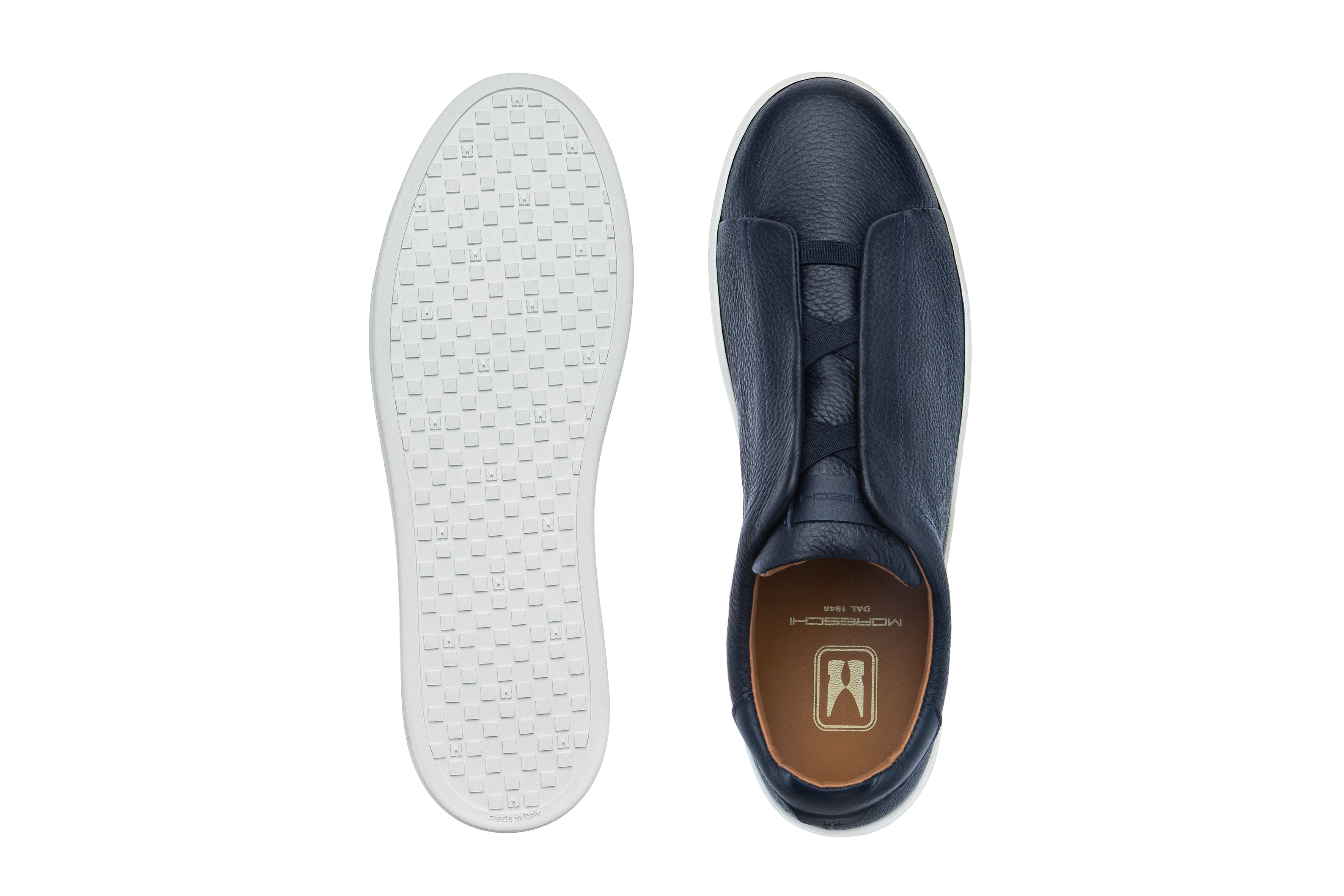 Dark blue textured leather slip-on sneaker with white sole. Elastic laces, tan insole with gold-toned logo, and grid-patterne