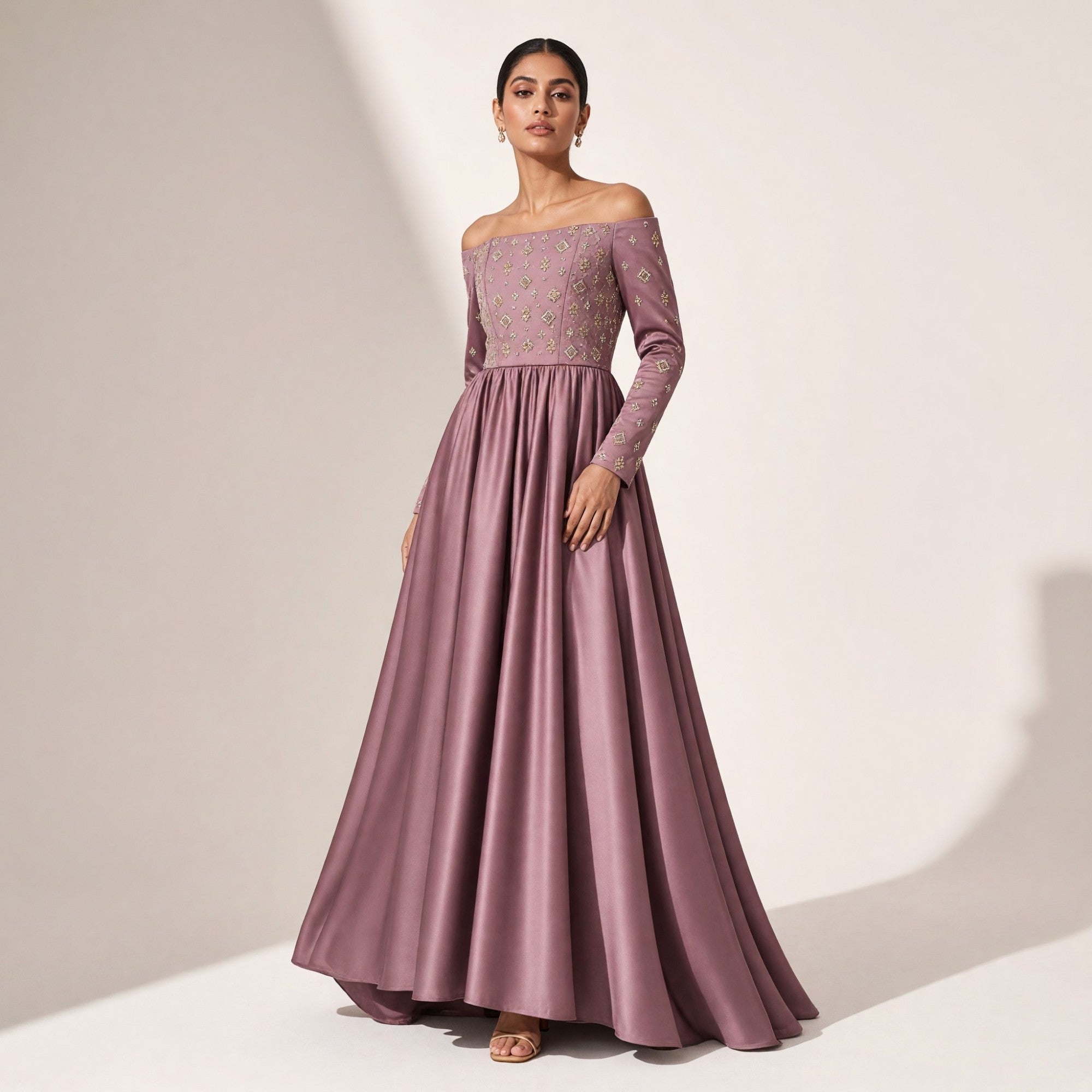 Mauve off-shoulder gown with long sleeves. Bodice and sleeves have gold-toned geometric embroidery. Full, flowing skirt.