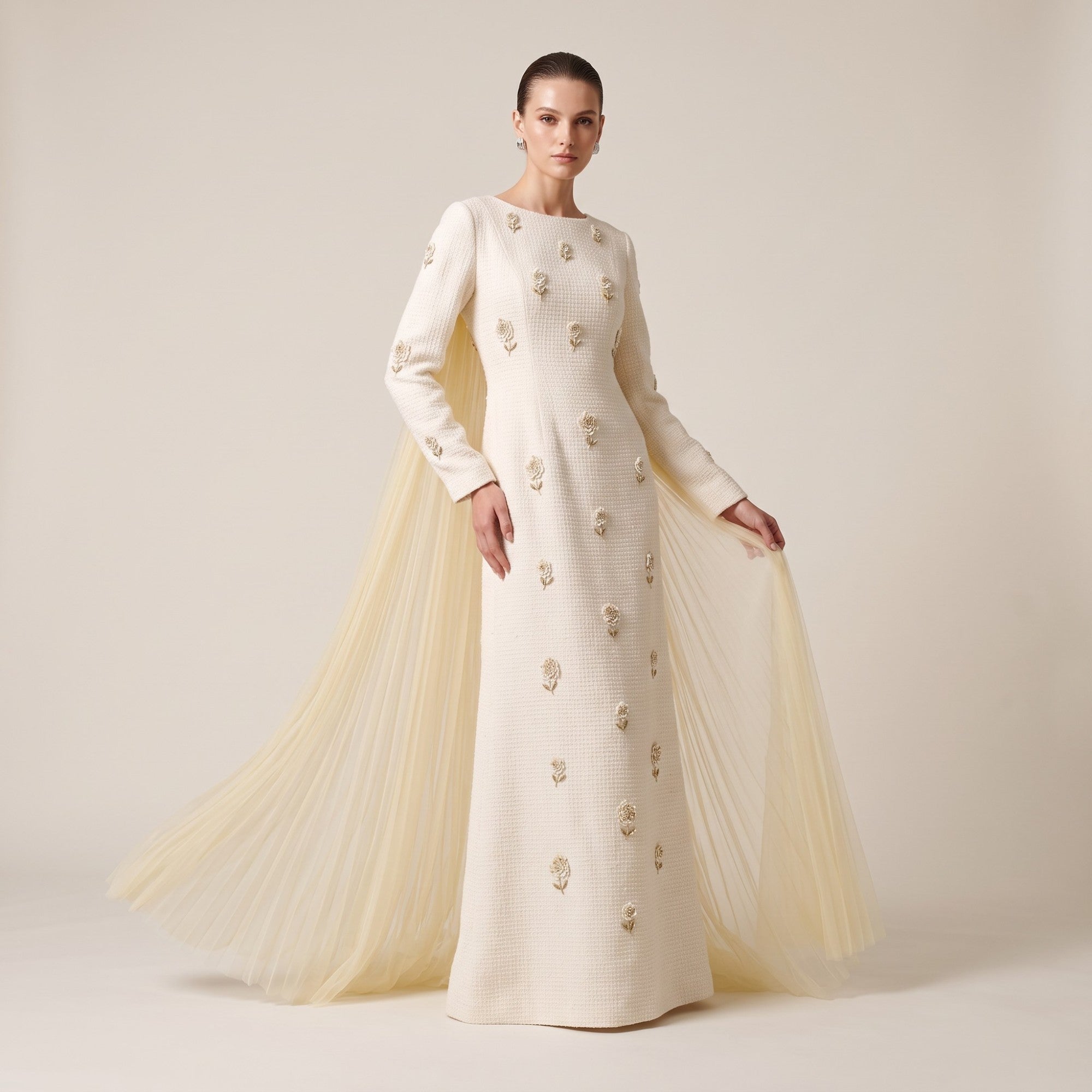 Off-white long-sleeved boat neck dress with gold-toned floral appliqués and a long, pleated, sheer cream cape.