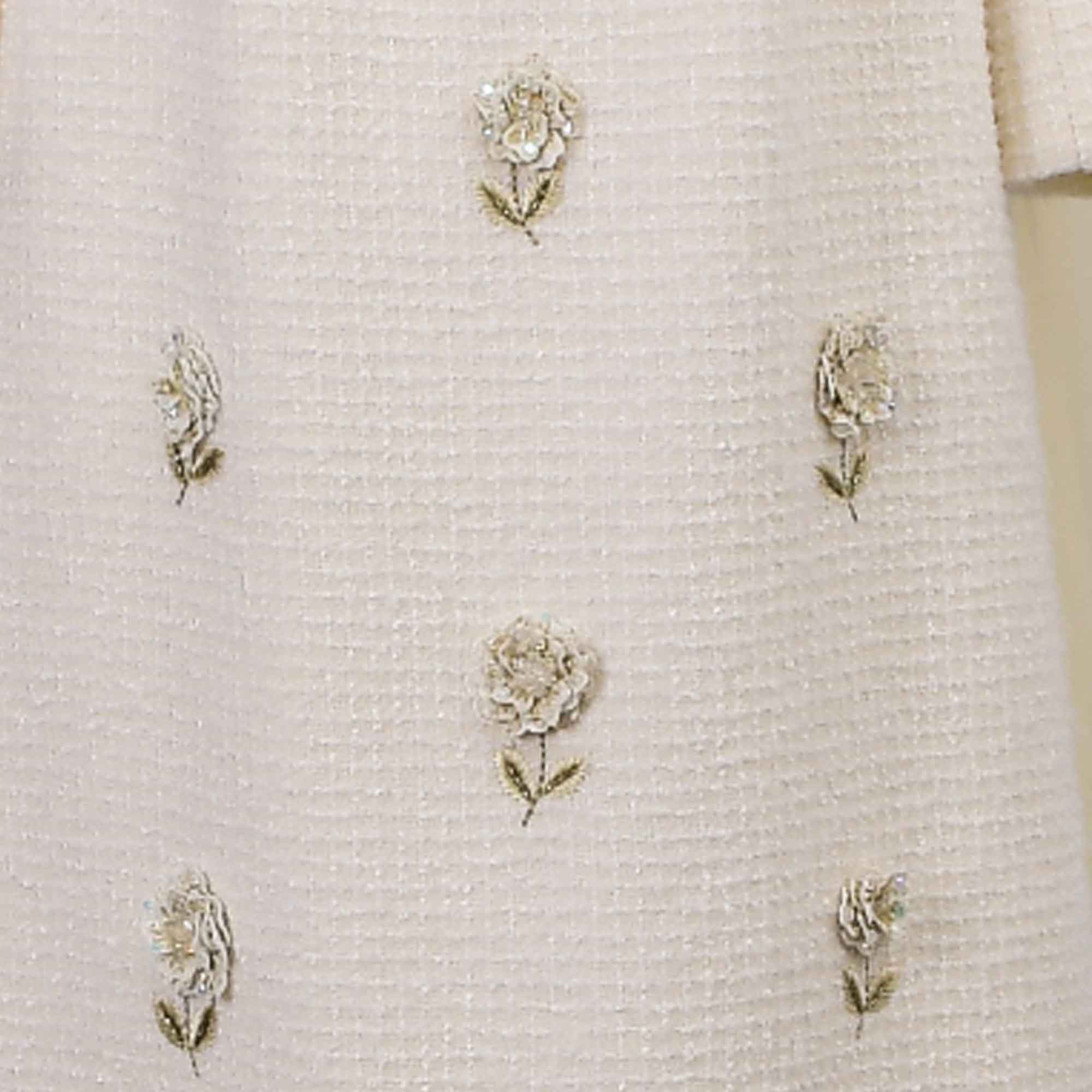 Off-white woven dress fabric with scattered beaded and sequined flowers with green embroidered stems.