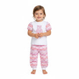 A cheerful baby girl model standing full-length while wearing the two-piece white and pink Missoni teddy bear chevron set against a plain background.