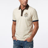 Lichen green short-sleeved polo shirt with dark brown collar and placket, and navy blue trim on ribbed cuffs, featuring an em