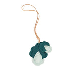 A handcrafted MUNI bag charm featuring layered dark green and light mint leather petals attached to a tan leather cord, isolated on a white background.