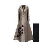 Front view of a Maison Darine champagne-bronze silk-satin abaya coat featuring a blazer collar, two buttons, and black 3D floral embroidery on the lower right side, shown with a black chiffon sheila.