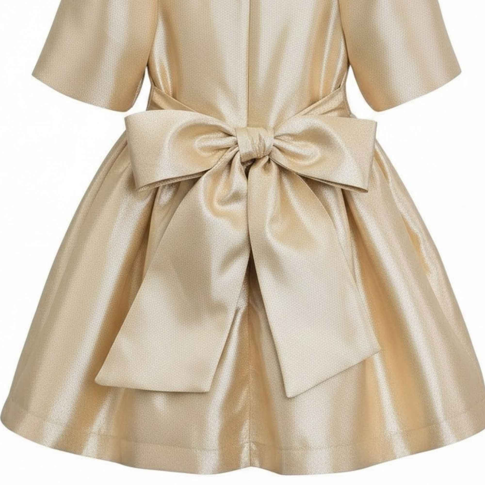 Detailed close-up view of the back of the Mamaluma gold dress, focusing on the texture of the shimmering metallic fabric and the construction of the large sash bow.