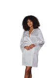 A woman with curly dark hair wearing a white satin robe with lace trim, standing in a modern gray interior room.