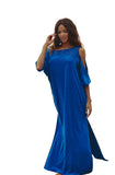 Woman in a blue dress standing on a beach with ocean and rocks in the background