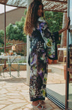 Woman in a floral outfit standing on a patio with outdoor furniture and plants.