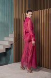 A model wearing a vibrant magenta pink sheer lace maxi dress with a matching belt and clutch, standing in a modern interior setting with a wooden slatted wall and concrete stairs.