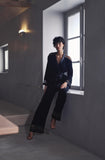 Model wearing Marjolaine dark velvet wrap jacket with matching trousers standing by window available at BLUE SALON.