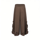 Front view of Meimeij brown wide-leg culotte trousers showcasing structural front pleats and detailed 3D fabric flowers along the outer side seams and hem against a white background.