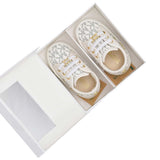 Front view of the packaging for Michael Kors baby shoes, showcasing a square white rigid gift box featuring a clear view window, silver brand lettering, and a white top handle.