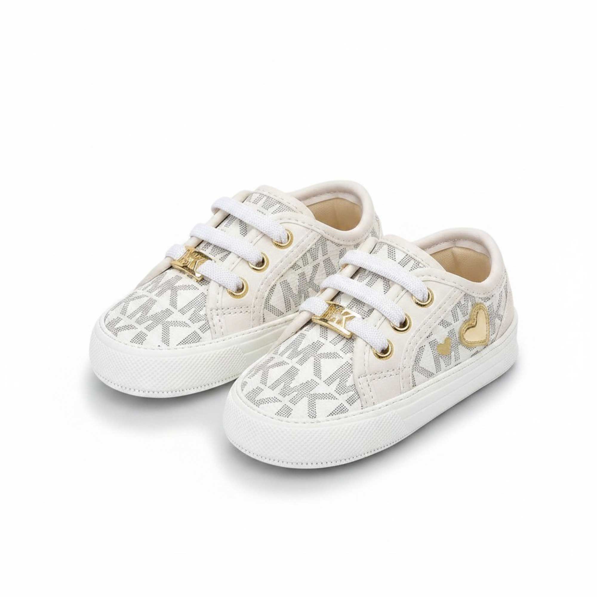 Angled side profile view of a pair of baby Michael Kors trainers, displaying an all-over grey monogram pattern and a stitched metallic gold heart outline on the outer side panel.