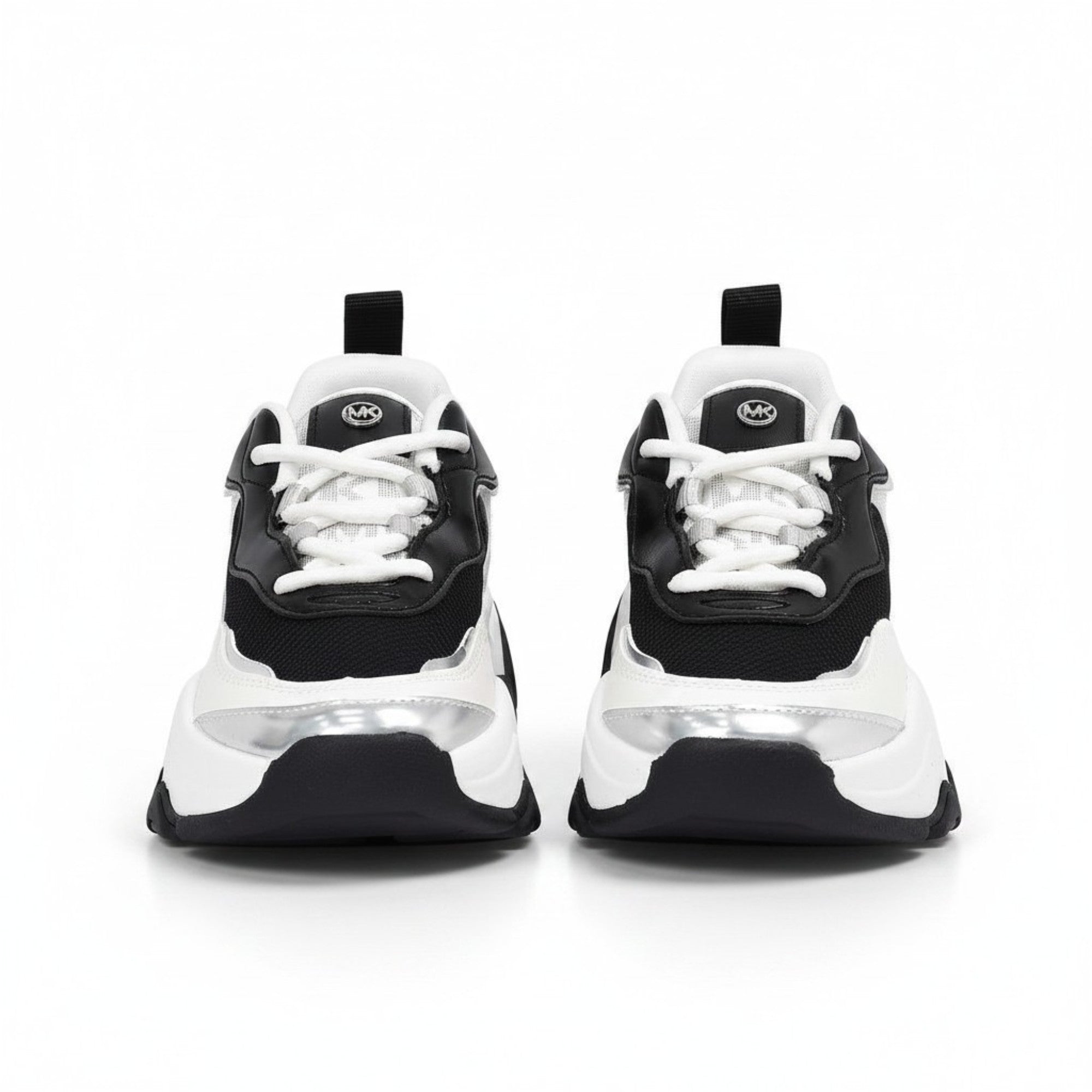 Straight front view of a pair of kids' chunky Michael Kors trainers, highlighting black faux-leather uppers, crisp white laces, and a small circular metallic MK crest logo on the tongues.