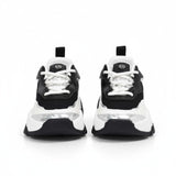 Straight front view of a pair of kids' chunky Michael Kors trainers, highlighting black faux-leather uppers, crisp white laces, and a small circular metallic MK crest logo on the tongues.