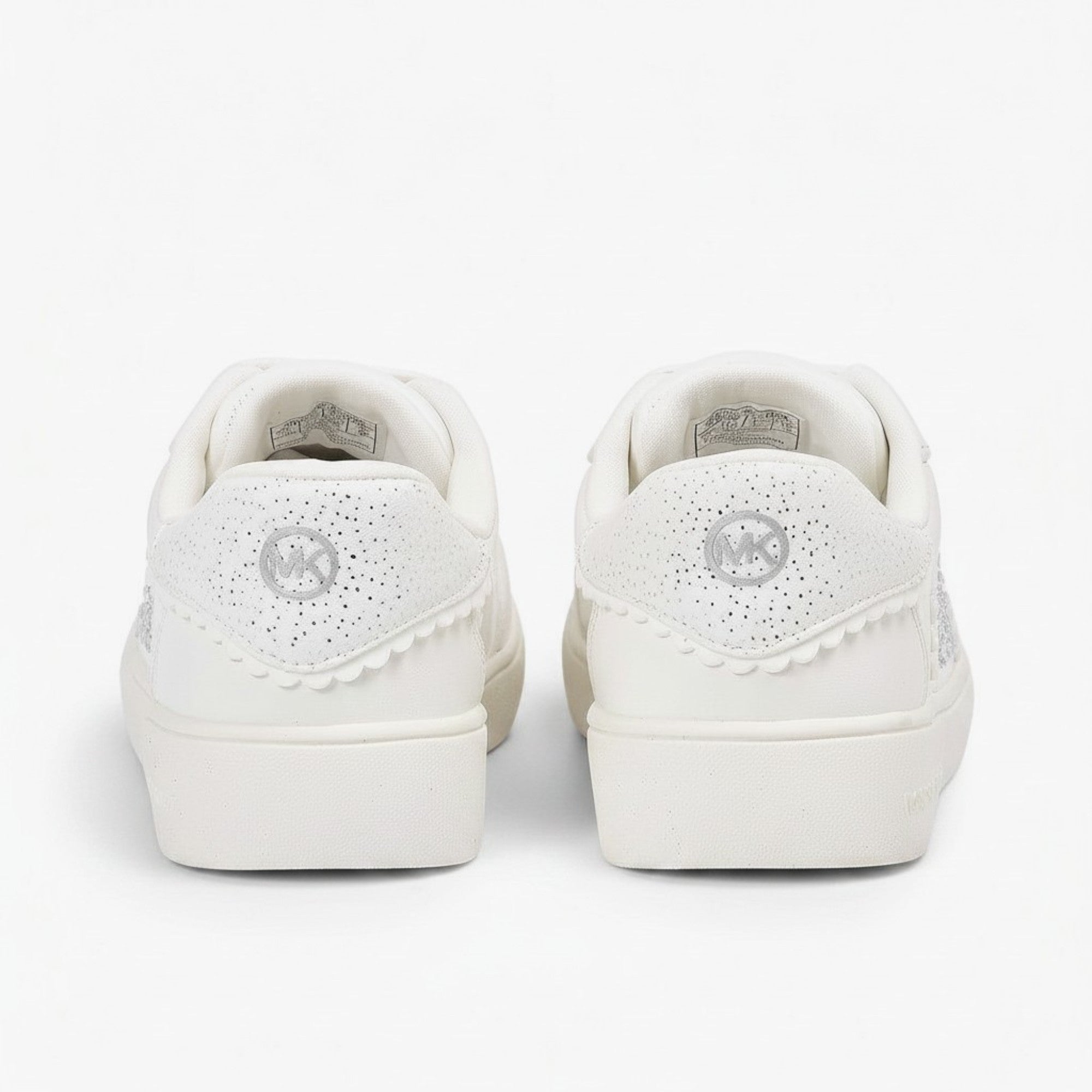 Rear heel view of a pair of kids' athletic sneakers, showing a white faux-leather back panel topped with a black pull loop and a small circular gold-tone MK badge.