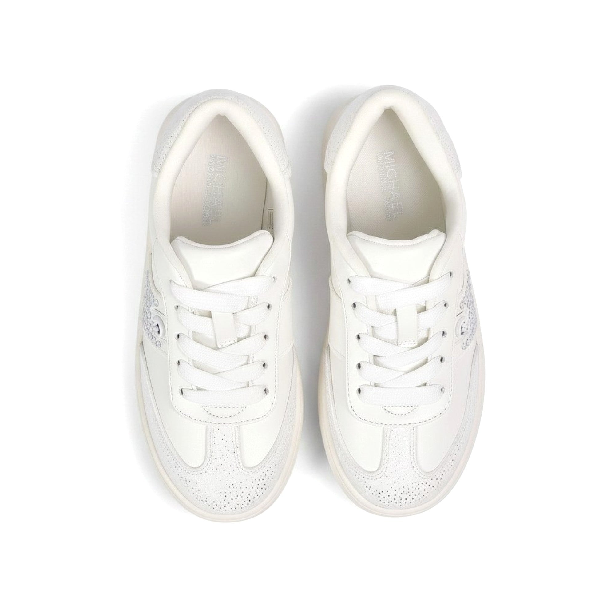 Directly overhead bird's-eye view looking inside a pair of kids' Michael Kors running shoes, showcasing black insoles with white printed logos and white athletic lacing.