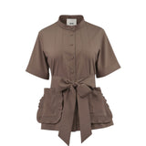 Front studio shot of a taupe brown short-sleeve Milva Mi blouse styled with its wide matching waist belt tied in a large bow, highlighting the ruffled patch pockets.