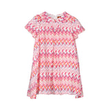 Front view of a short-sleeved Missoni baby girl dress showcasing an all-over pink, orange, and purple zigzag pattern, a Peter Pan collar, and a decorative front bow.