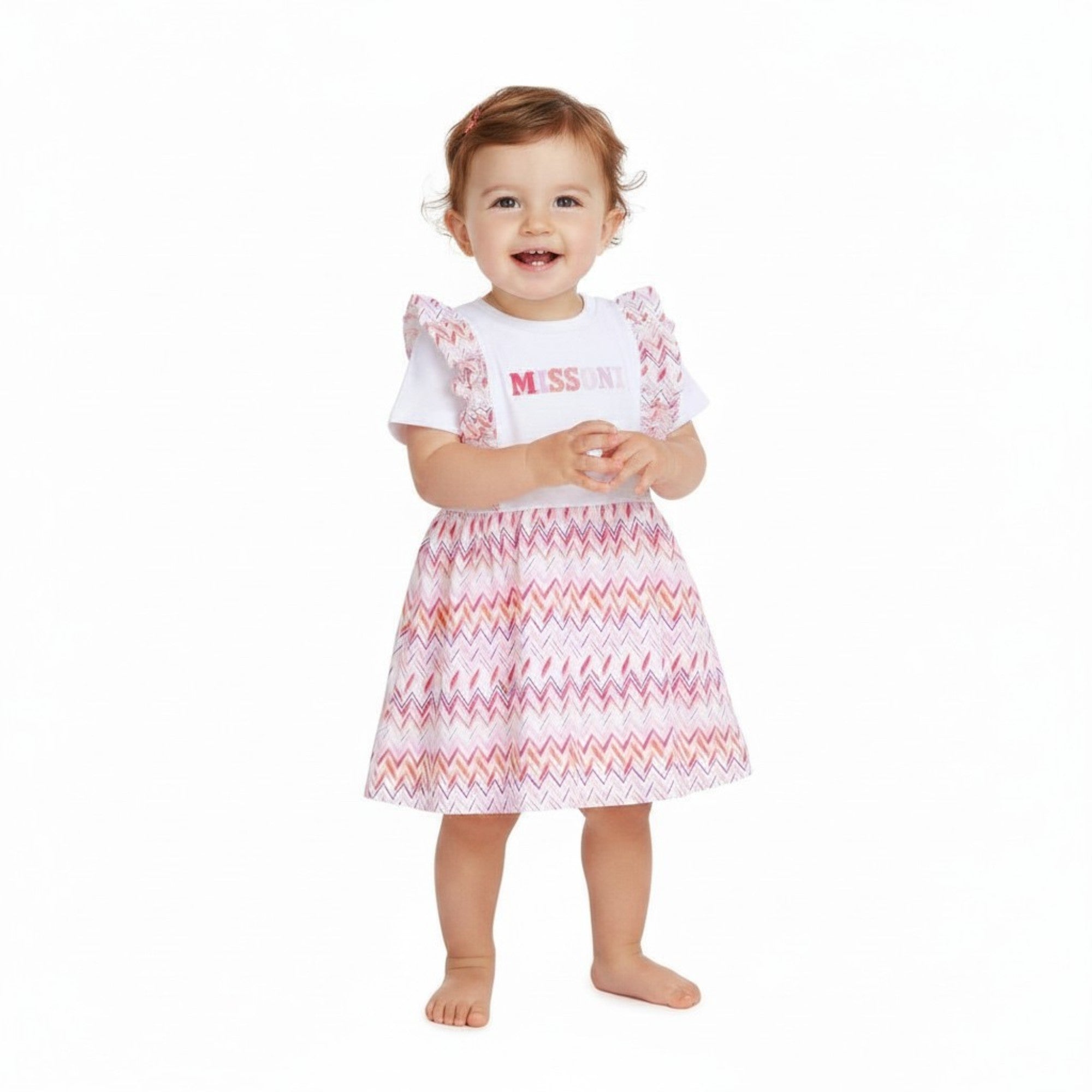 A smiling baby girl model wearing the white and pink Missoni zigzag ruffle dress against a plain white background.